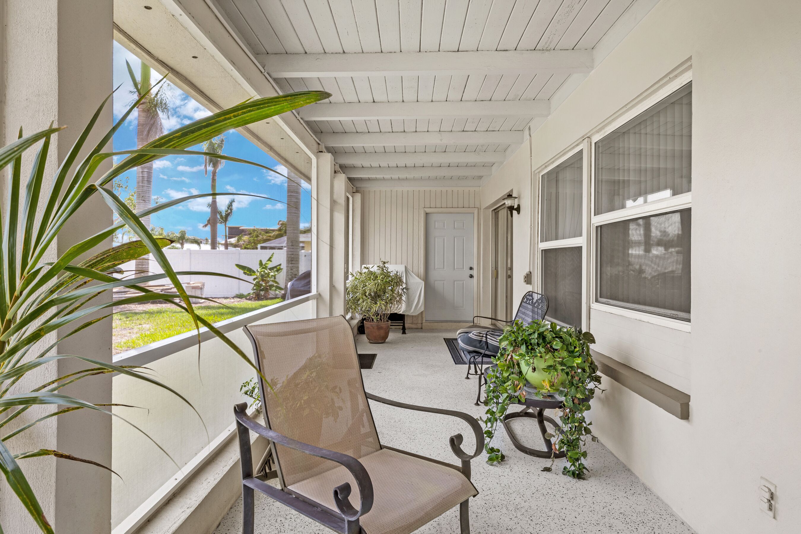A covered porch with a chair, a potted plant, and a view of the outdoors.