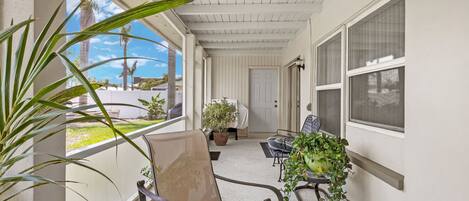 A covered porch with a chair, a potted plant, and a view of the outdoors.