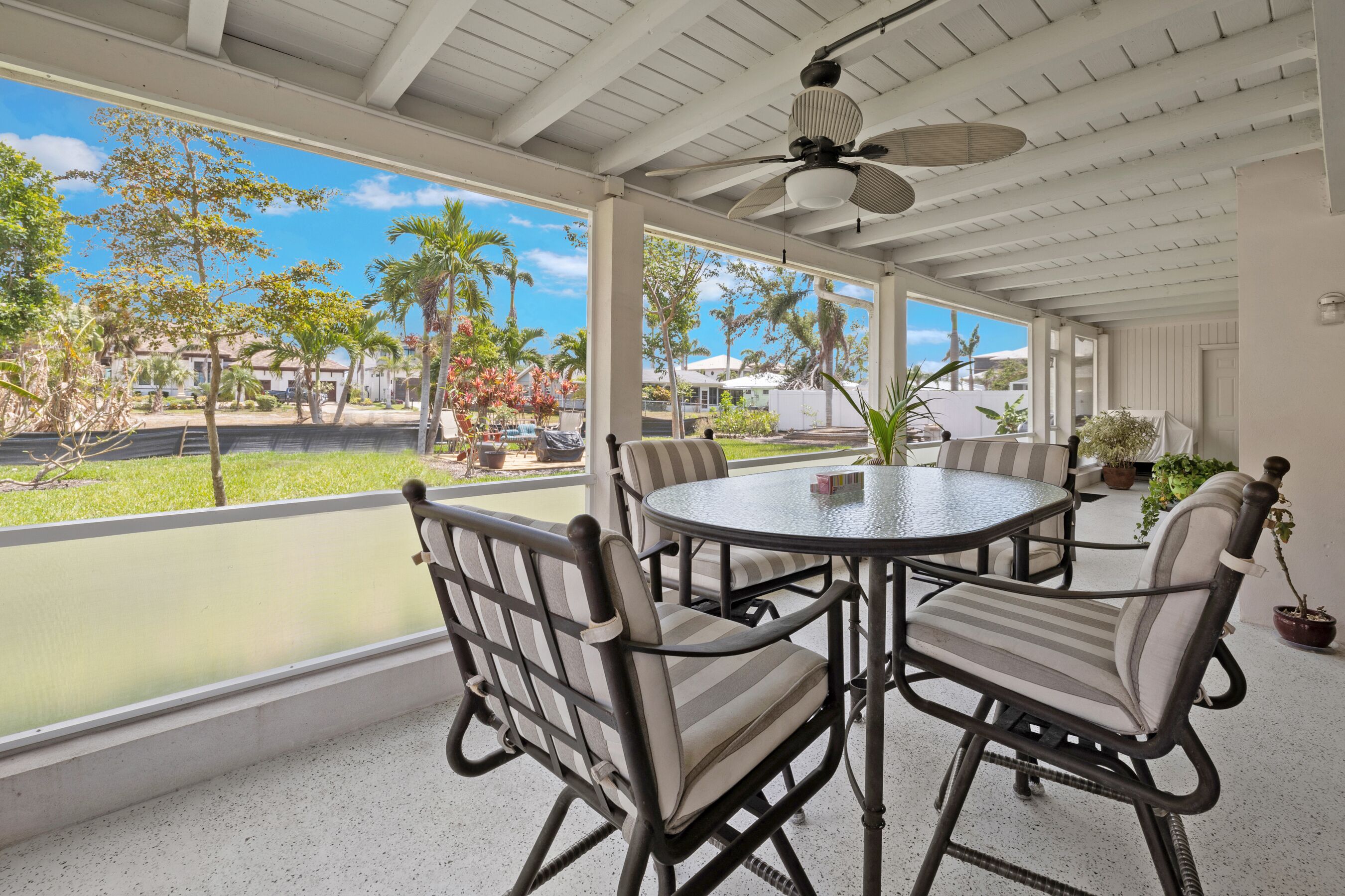 A covered outdoor patio with a round table and chairs, large windows, and ceiling fans.
