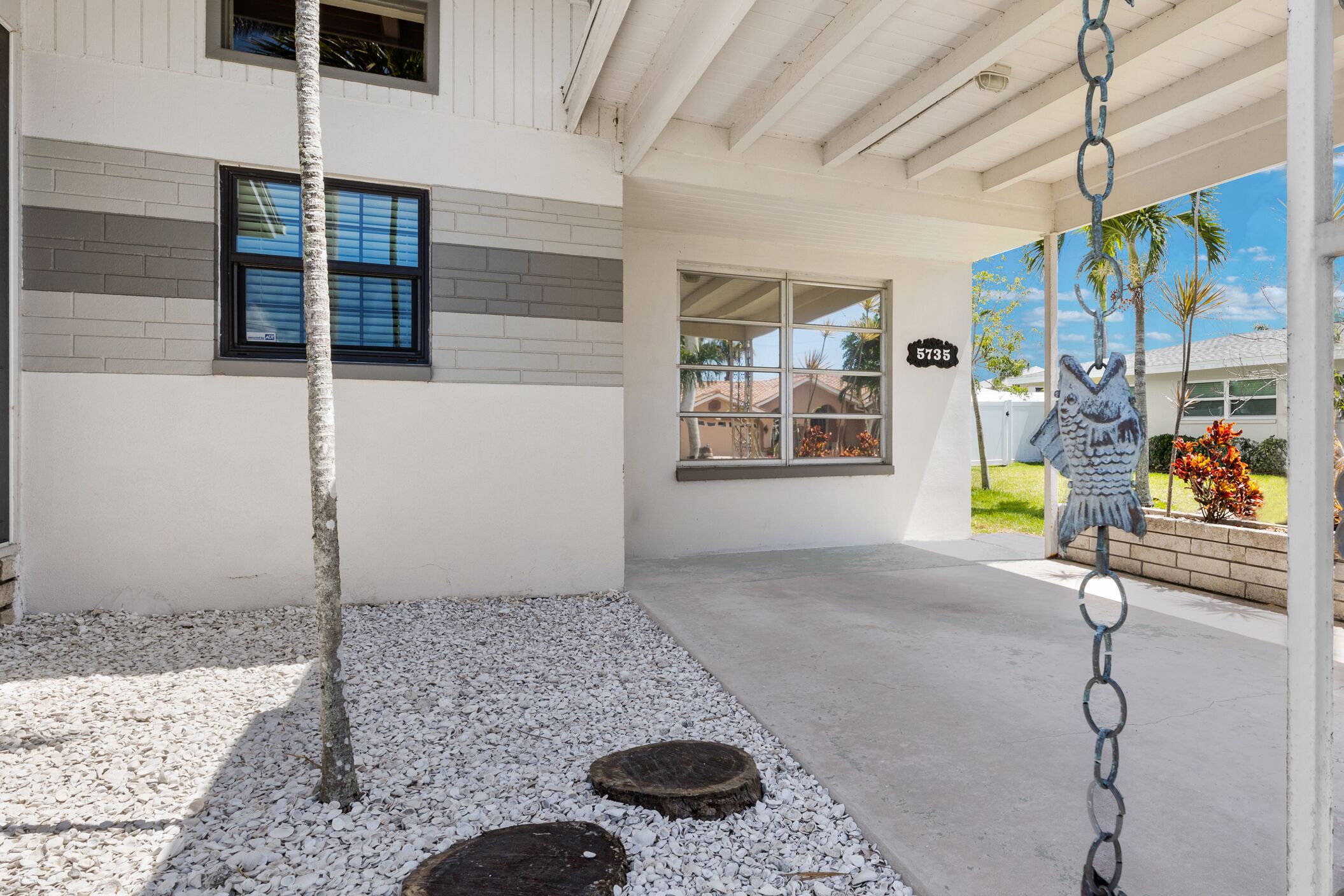 A modern building with a covered patio area, a tree, and a decorative fish sculpture.