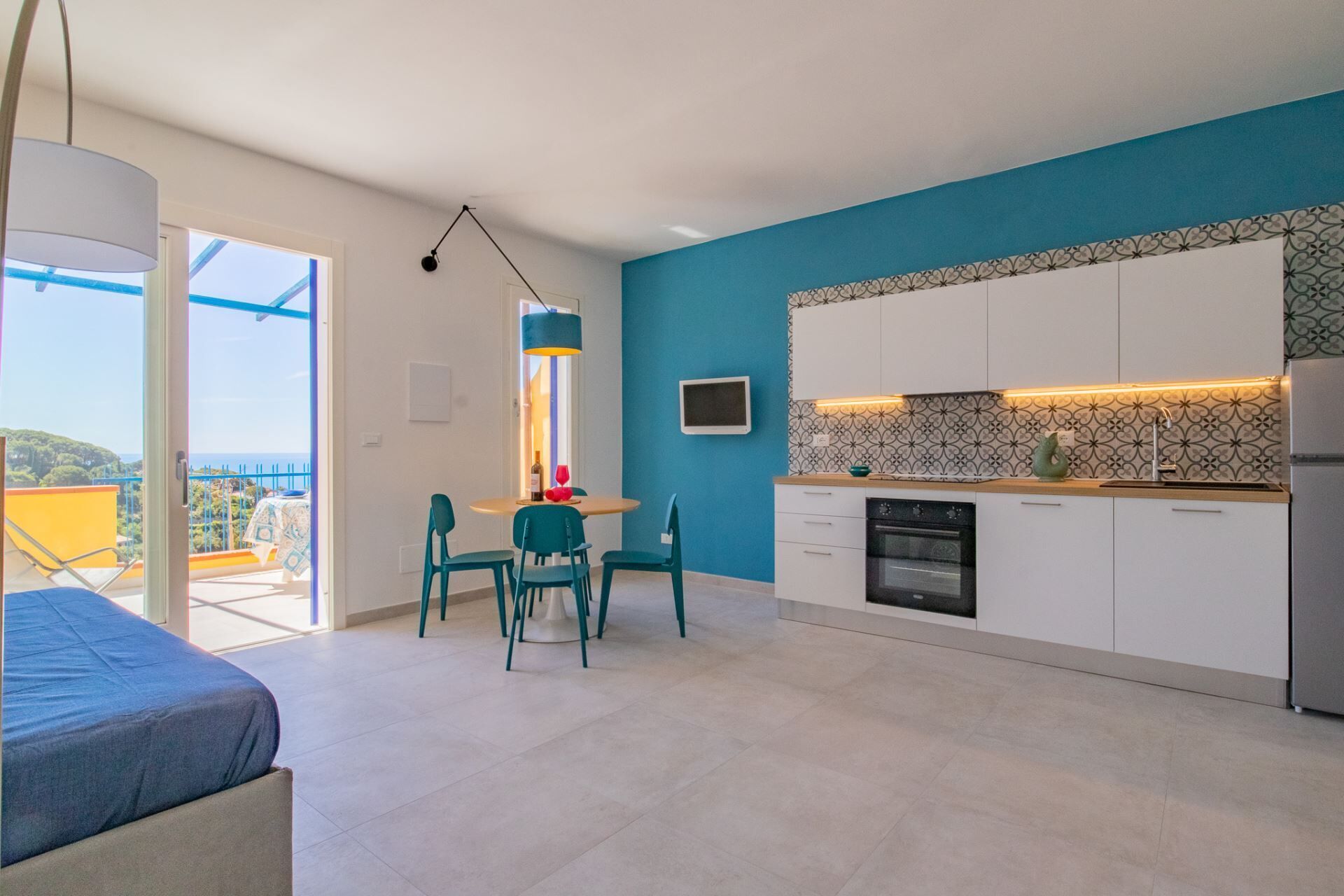 Une cuisine moderne avec des meubles blancs, un mur d’accent bleu et un coin repas avec des chaises turquoise.