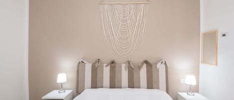 A bedroom with a large bed, two bedside tables with lamps, and a wall-mounted macrame piece above the bed.