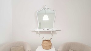 Ein Zimmer mit zwei beigen Sesseln, einem weißen Tisch mit einem gewebten Korb und einem weißen, an der Wand befestigten Spiegel.
