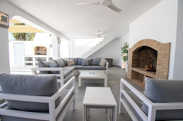 A modern living room with a sectional sofa, white furniture, a fireplace, and a staircase leading to an outdoor area.