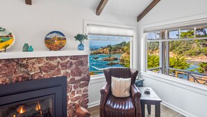 A room with a stone fireplace, a leather chair with a cushion, and a view of the ocean through large windows. - Buckhorn Cove Ocean Front with Private Peninsula (Little River)