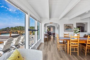 Un vaste espace dédié à la salle à manger, offrant une vue sur l’océan, avec des meubles en bois et une grande fenêtre donnant sur la terrasse.