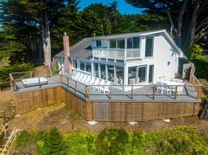 Une maison à deux étages dotée d’une terrasse, d’un espace salon extérieur et d’un jacuzzi.