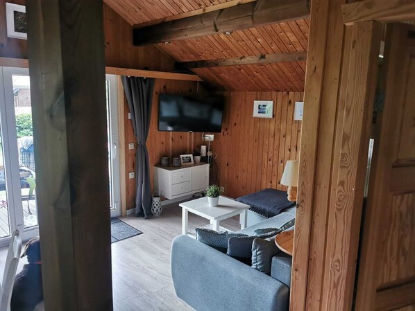 Ein gemütliches Zimmer mit Holzbalkendecke, einer Couch, einem kleinen Tisch und einem an der Wand befestigten Fernseher.