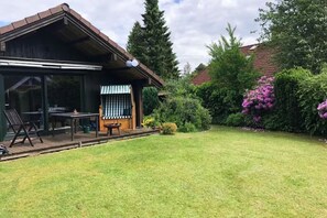 Ein Haus mit überdachter Terrasse, Rasen und umgebender Bepflanzung.