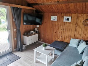 Ein gemütliches Blockhaus-Interieur mit Holzbalkendecke, einem weißen Sofa, einem kleinen Tisch und einem an der Wand befestigten Fernseher.