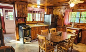 A wooden cabin kitchen with a stove, refrigerator, wooden cabinets, and a dining table with chairs.