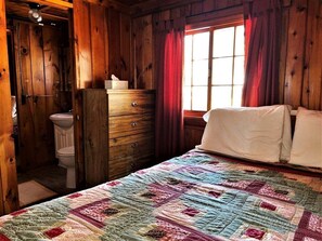 Une pièce en bois avec un lit, une commode, une fenêtre avec des rideaux et des toilettes.
