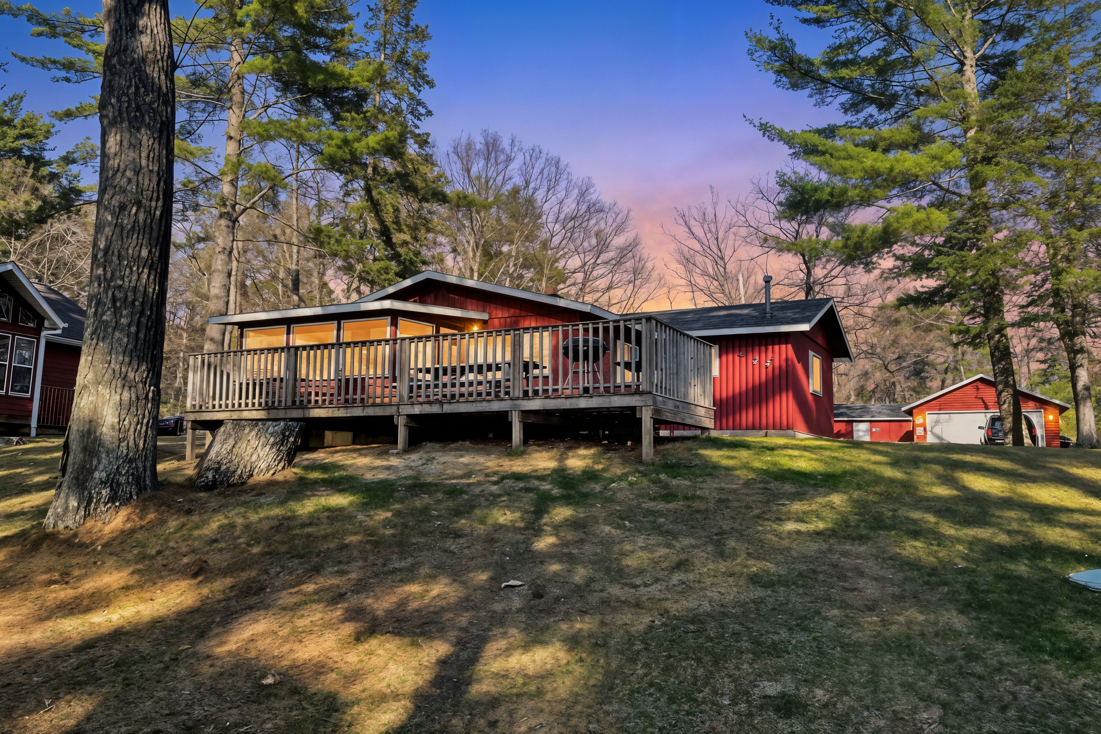 A cabin with a deck, surrounded by trees and a clear sky.