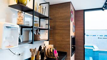 A modern kitchen with a coffee machine, wooden utensils, and a view of a swimming pool.