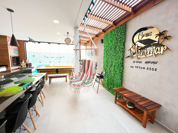 A modern restaurant interior with a green wall, wooden furniture, and a hanging chair.