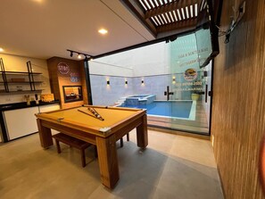 Una mesa de billar en una habitación con vistas a una piscina, visible a través de un ventanal.