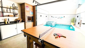 A modern kitchen with a wooden table and a ping pong table, a small pool, and a stop sign on the wall. - Casas Marimar Ilheus (Caraguatatuba)