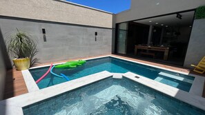 Una piscina con un juguete inflable pequeño, una planta en maceta y vistas a un espacio interior con una mesa y sillas.