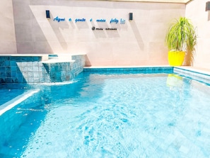 A swimming pool with clear blue water, a tiled wall with a welcoming message, and a potted plant.