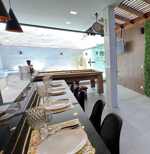 Un comedor con una mesa larga dispuesta para una comida, una mesa de billar y vistas al cielo.