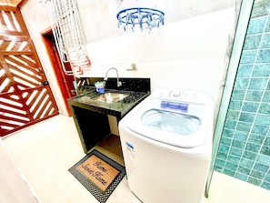 A compact bathroom with a sink, a washing machine, and a shower area.