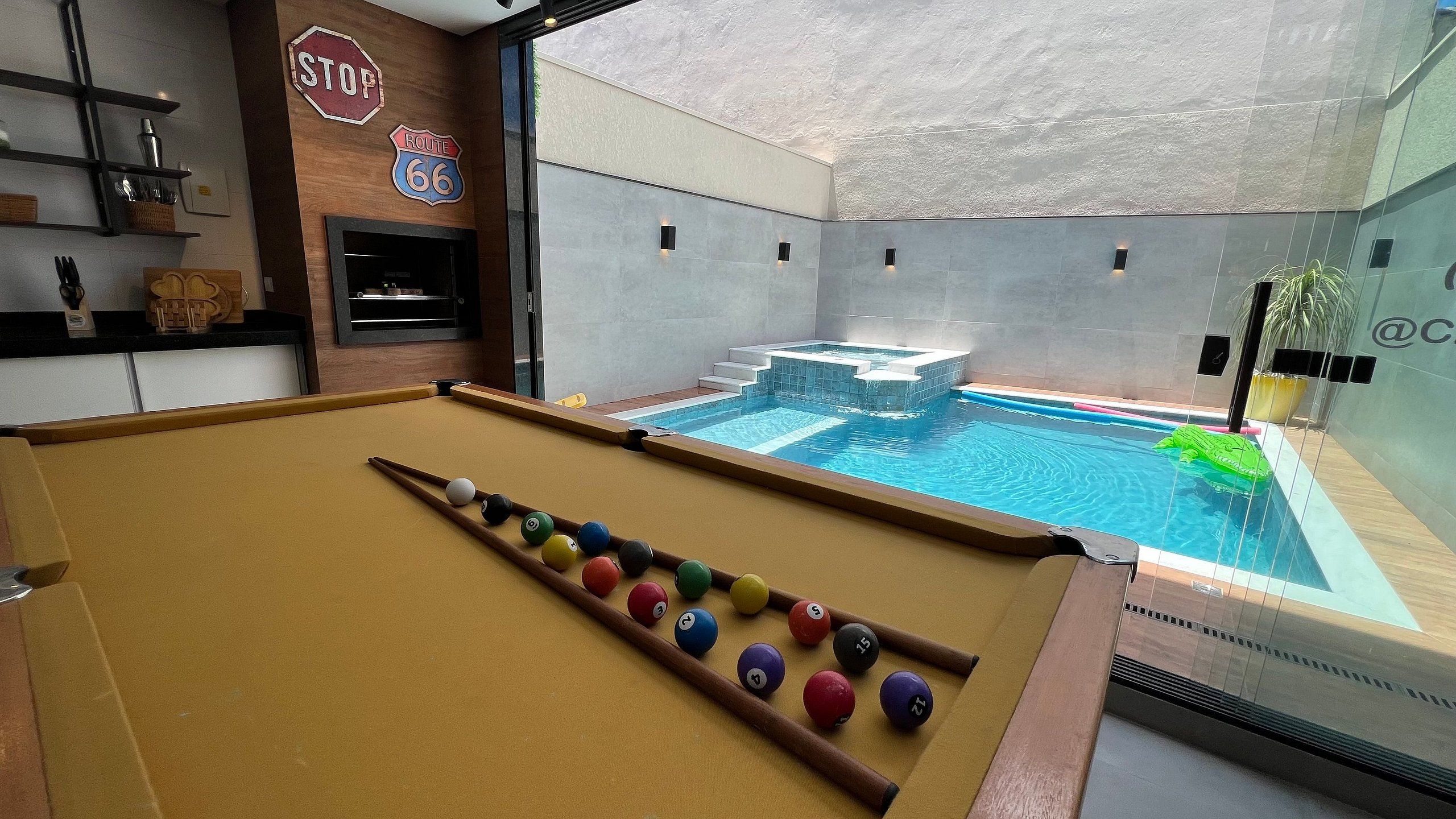 Una mesa de billar con bolas, otra mesa de billar y una mesa pequeña de billar en una habitación con vistas a una piscina.