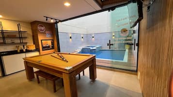 A pool table in a room with a view of a swimming pool through a glass door.