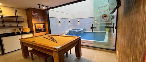 A pool table in a room with a view of a swimming pool through a glass door.
