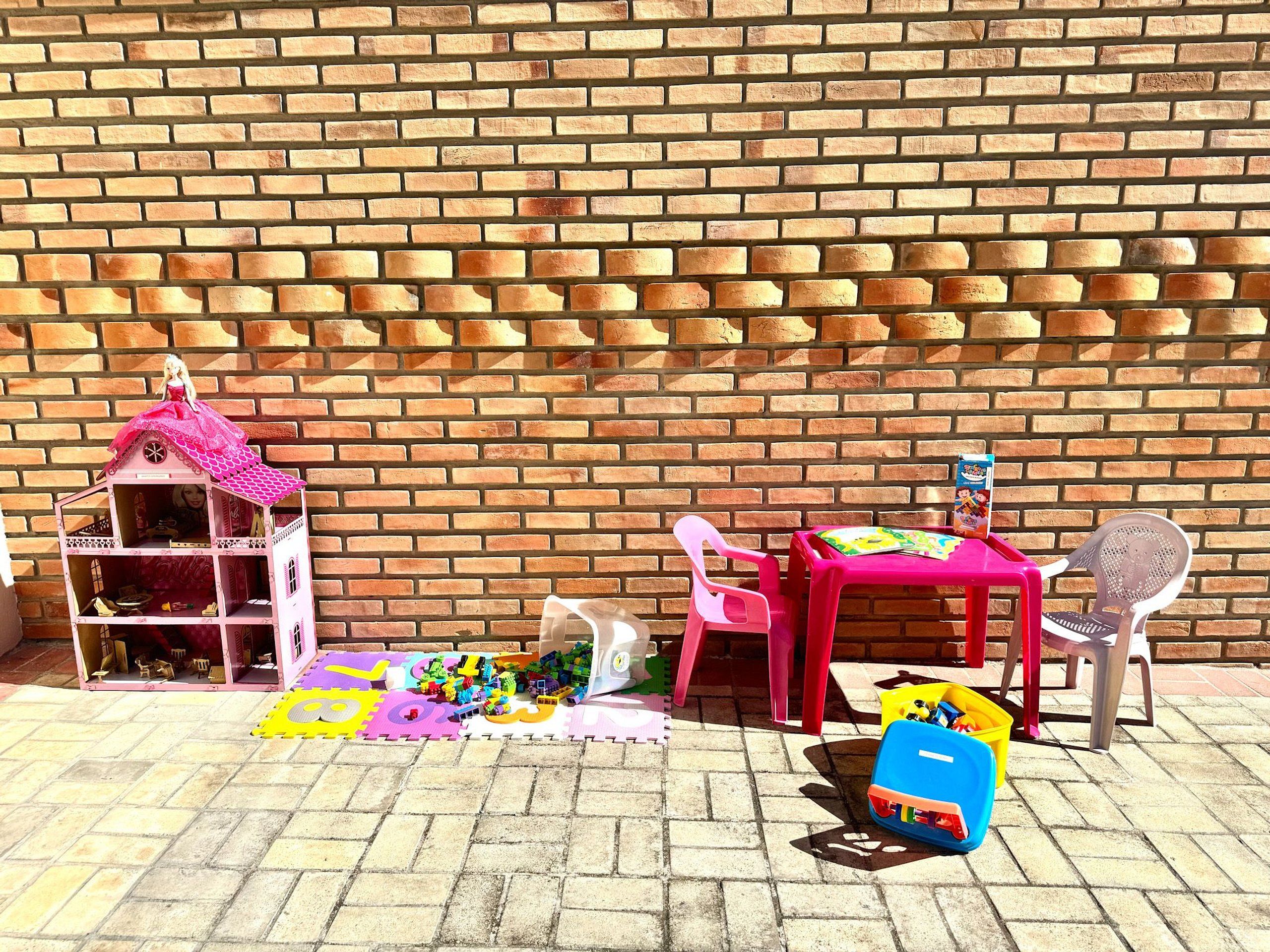 A brick wall with a dollhouse, a table with chairs, and scattered toys.