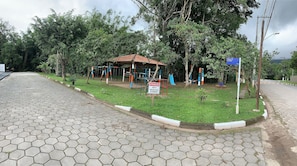 A playground with a small shelter, surrounded by trees and a paved area.