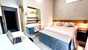 A hotel room with a large bed, a desk with a laptop, a mirror, and a bedside table with a lamp. - Casas Marimar Ilheus (Caraguatatuba)