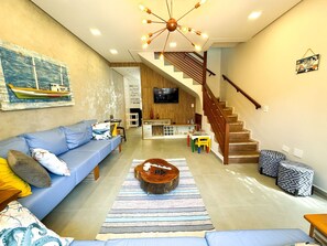 Una sala de estar moderna con un sofá azul, una mesa de centro de madera y una escalera que lleva a un nivel superior.