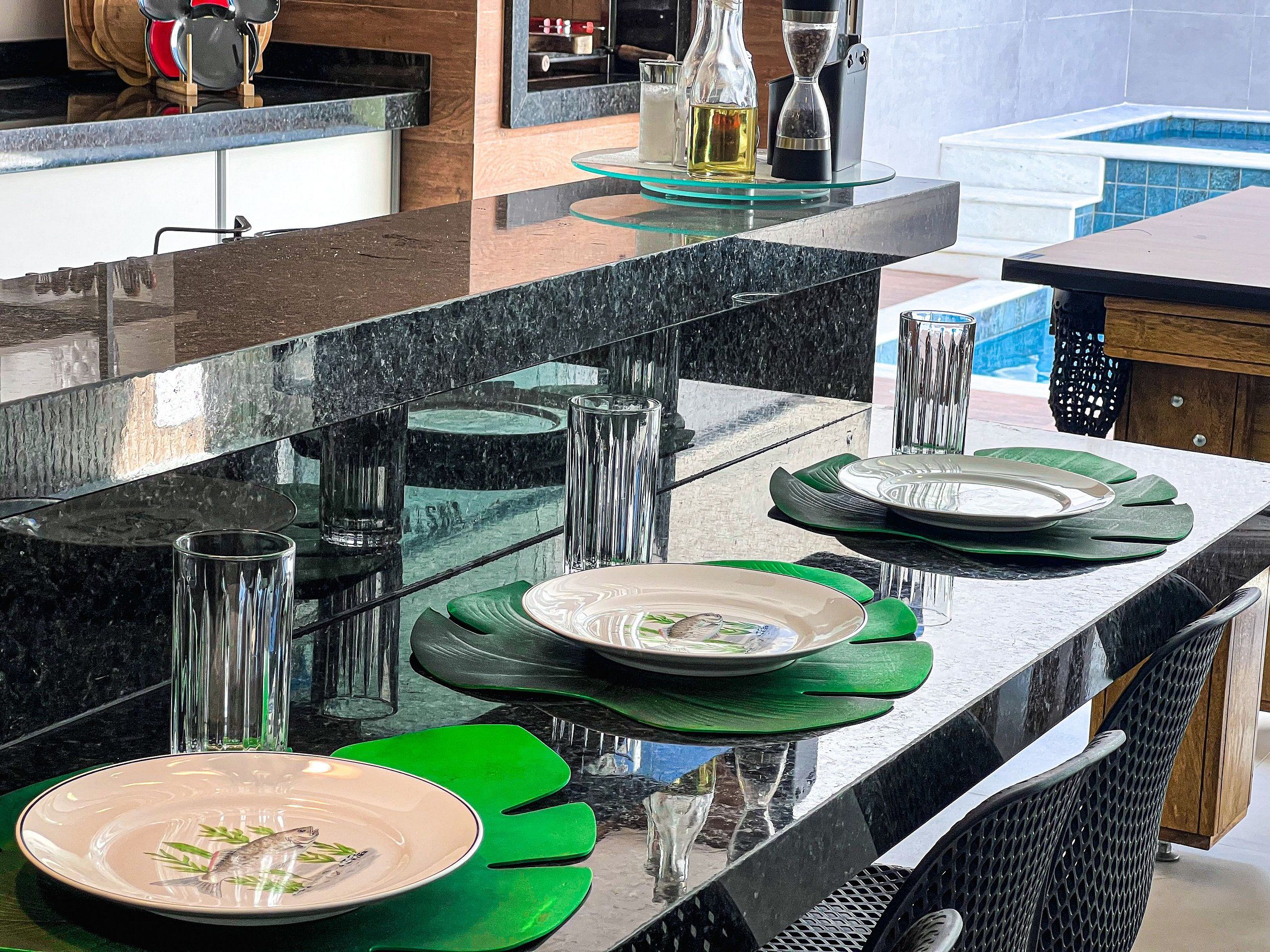 A modern kitchen with a granite countertop, green placemats, and a fish design on a plate.