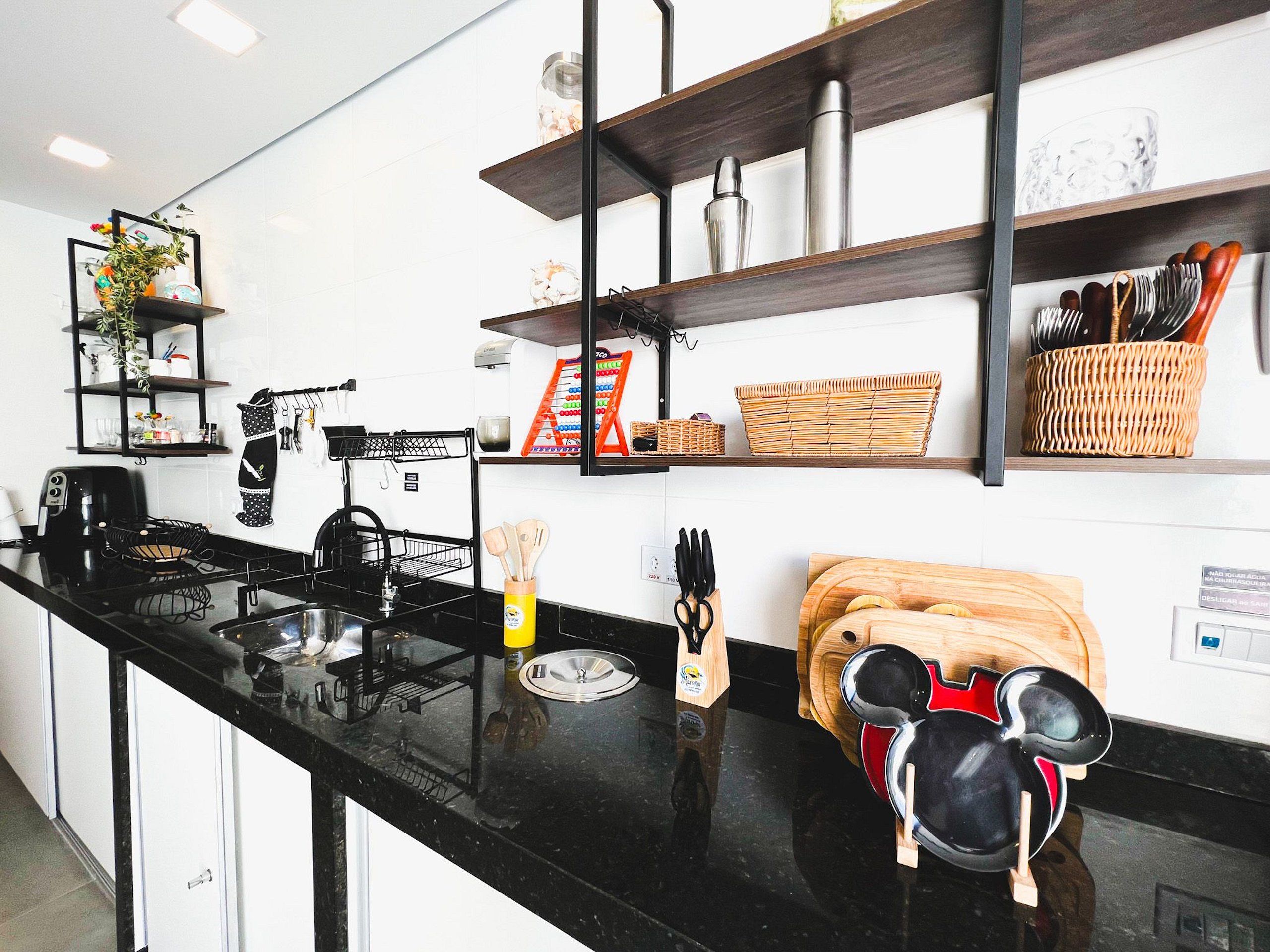 Une cuisine moderne avec des plans de travail noirs, une machine à café, une bouilloire et divers ustensiles rangés sur des étagères.