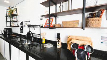 Une cuisine moderne avec des plans de travail noirs, une machine à café, une bouilloire et divers ustensiles rangés sur des étagères.