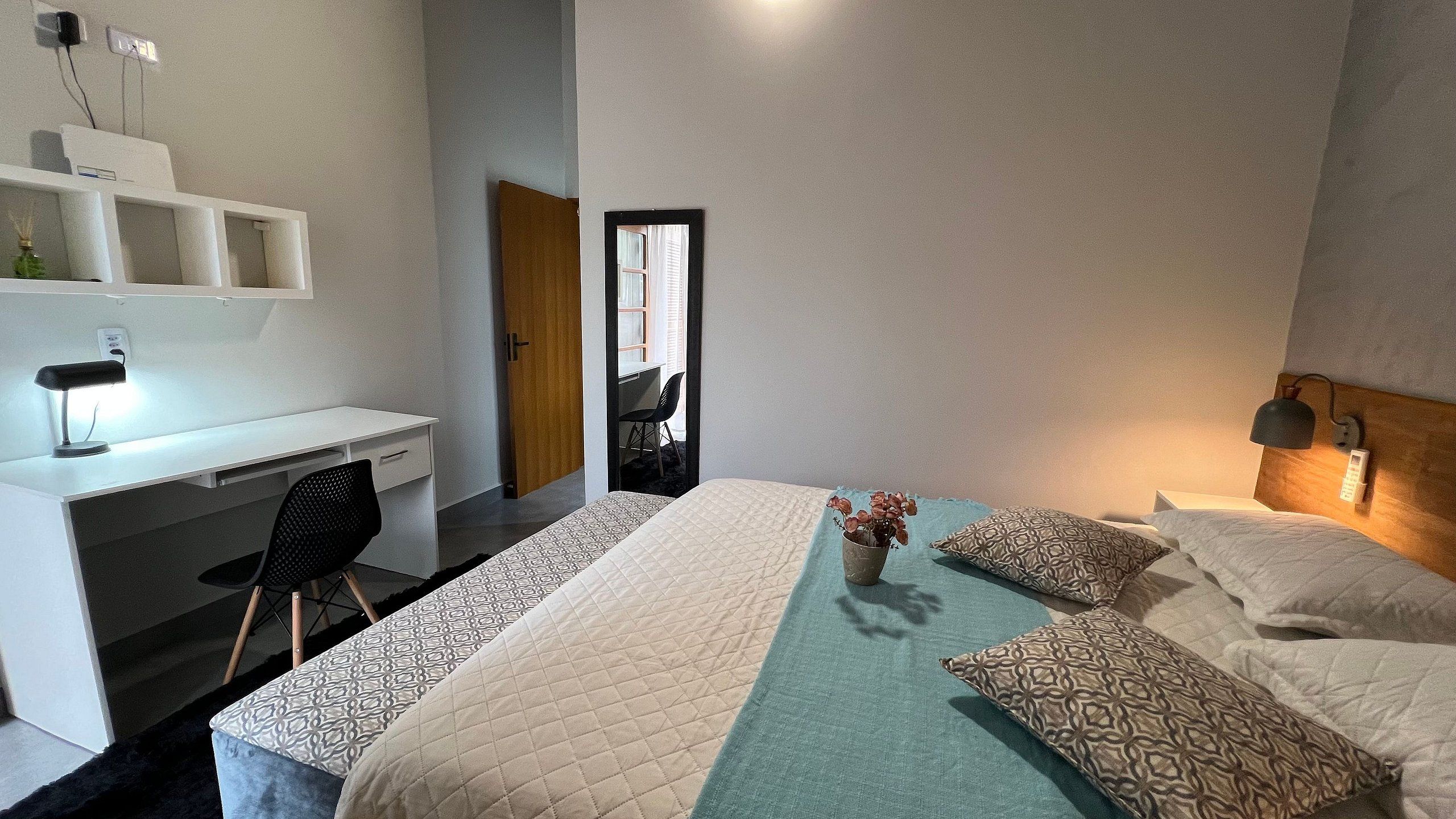 Quarto de hotel moderno com cama, abajures, escrivaninha e uma cadeira.