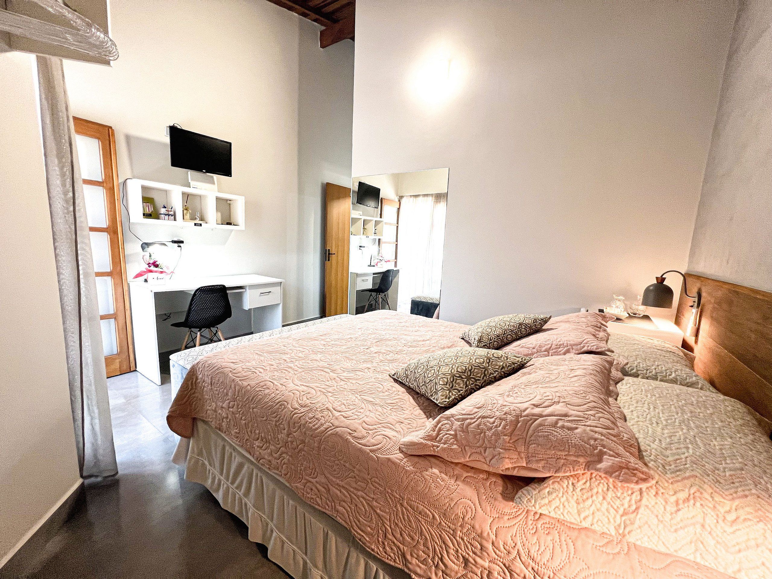 A bedroom with a large bed, a desk, and a TV mounted on the wall.