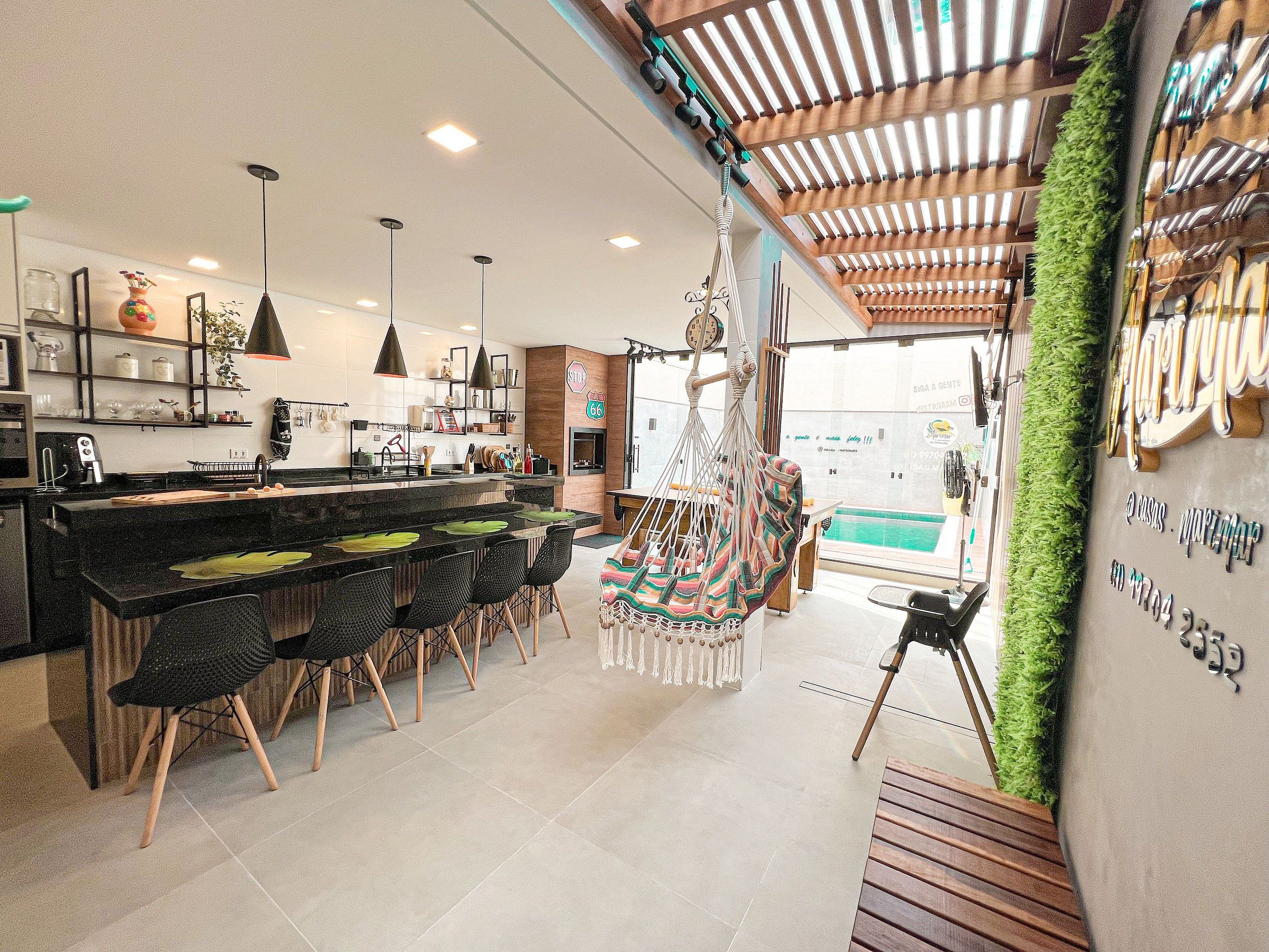 A modern kitchen with a bar area, hanging chairs, and a view of the pool.