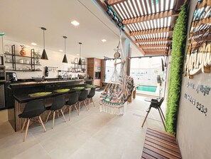 A modern kitchen with a bar area, hanging chairs, and a view of the pool.