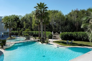 A swimming pool with palm trees and a fence, surrounded by greenery.