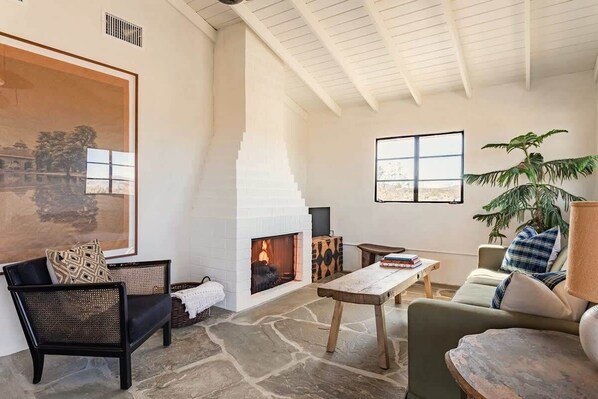 A cozy living room with a fireplace, comfortable seating, and a large painting on the wall.