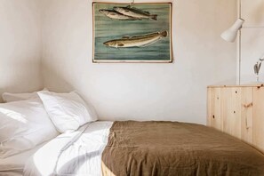 Un dormitori amb un llit, un panell de capçal de fusta, una làmpada penjada a la paret i una il·lustració d'un peix emmarcada.