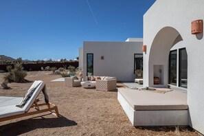 A modern outdoor patio with lounge chairs and a seating area, surrounded by a desert landscape.