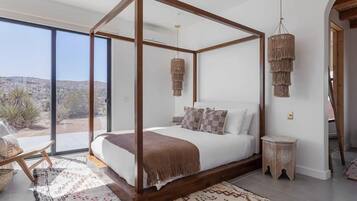 Quarto com cama de dossel, vista através de amplas janelas e luminária pendente.