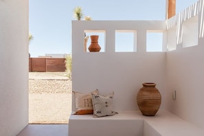 Un interior moderno con una pared blanca, una gran maceta de barro y dos cojines con diseños geométricos.