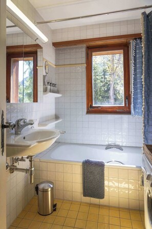 Ein Badezimmer mit zwei Waschbecken, einer Badewanne, einem Fenster und einem Handtuchhalter.