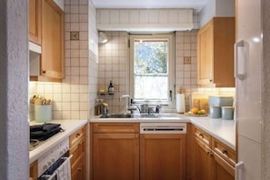 A kitchen with wooden cabinets, a white countertop, a window, and a dishwasher. - 3BR Central: Pool, Sauna, Gym & Views (Verbier)
