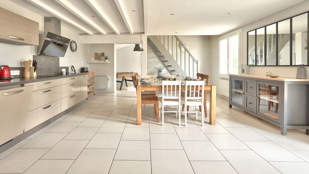 Una cocina moderna con comedor, que cuenta con una isla grande, electrodomésticos integrados y una escalera que sube a otro nivel.