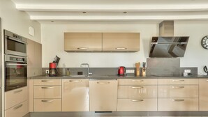 Una cocina moderna con electrodomésticos integrados, una campana extractora de acero inoxidable y un ventanal sobre el fregadero.