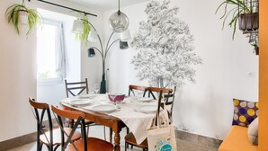 A dining area with a table set for four, surrounded by wooden chairs, a hanging plant, and a wall-mounted lamp. - Stunning 4* Home for 6, Beach & Port Walkable (Le Guilvinec)